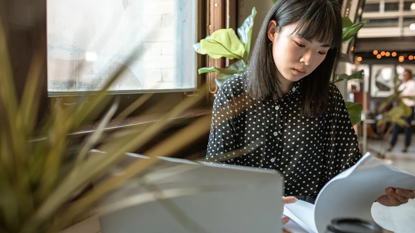 Perempuan bekerja menggunakan laptop sambil memeriksa dokumen